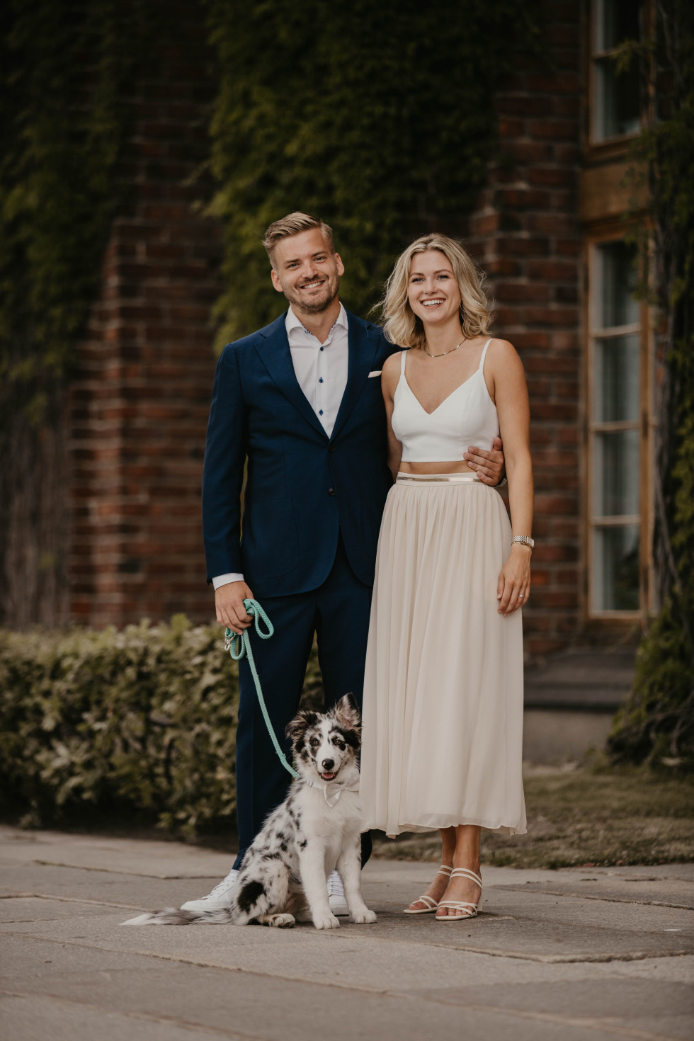 Bröllopsgäster poserar med sin hund, vackert klädd för bröllopet, under ceremonin.