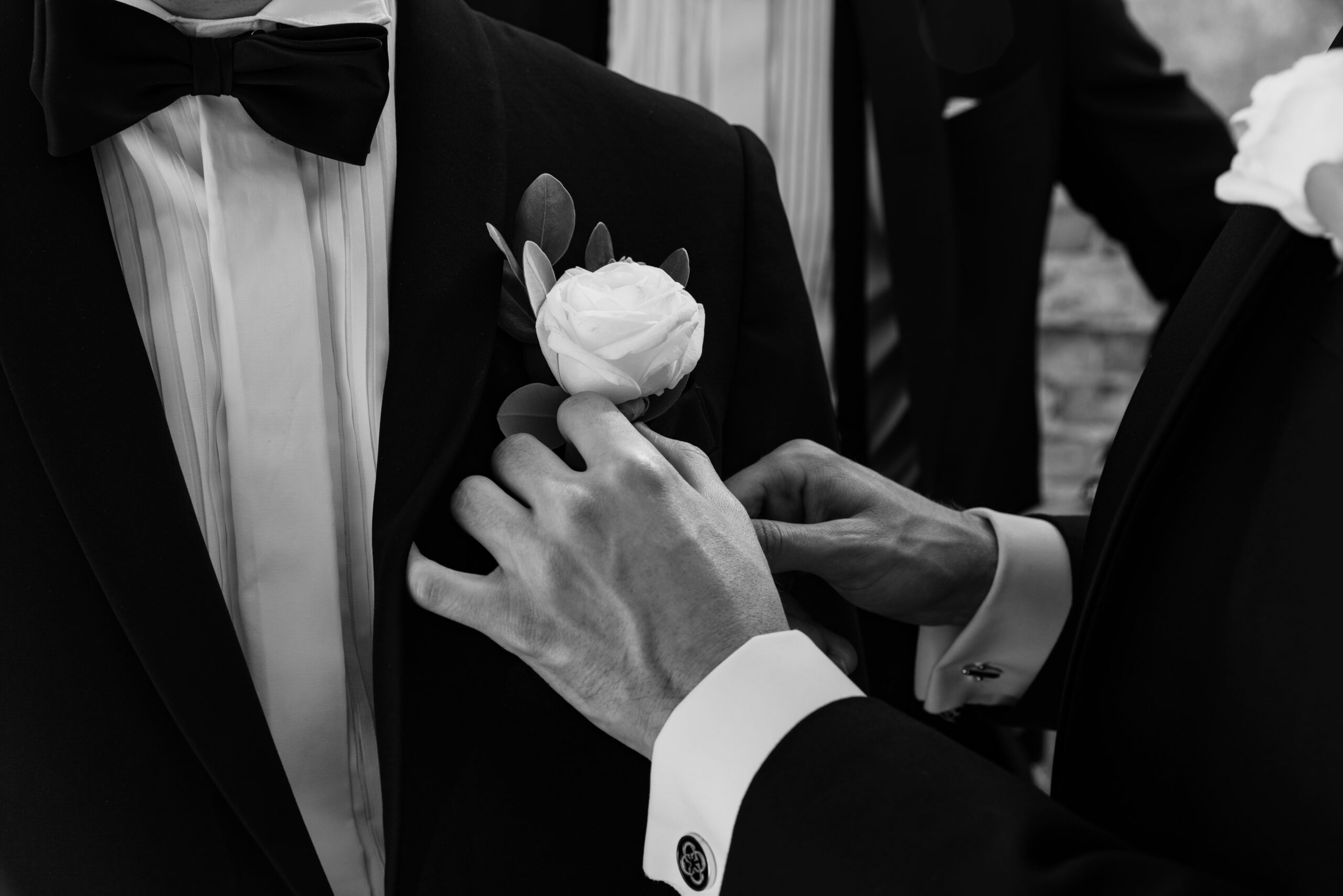 Närbild på en hand som fäster en blommig corsage på slaget av en elegant bröllopskostym.